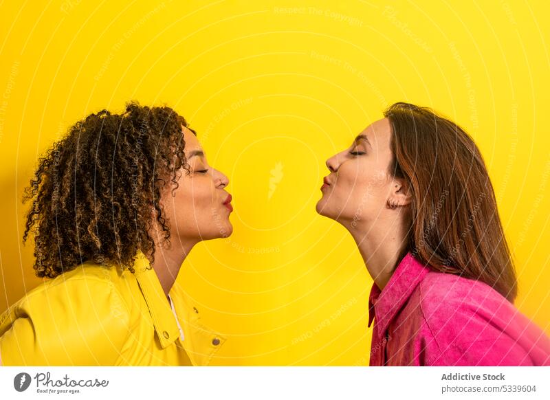 Happy multiethnic friends kissing each other on yellow background women together cheerful smile happy love air kiss relationship girlfriend young diverse