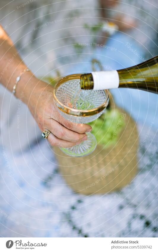 Crop person pouring champagne in glass picnic alcohol prepare nature celebrate drink beverage bottle countryside holiday summer event weekend serve booze