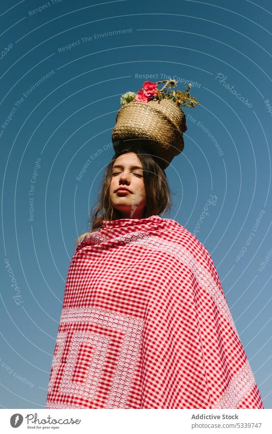 Calm woman with wicker basket on head dreamy flower plaid nature eyes closed countryside carefree checkered blue sky young summer cloudless peaceful flora