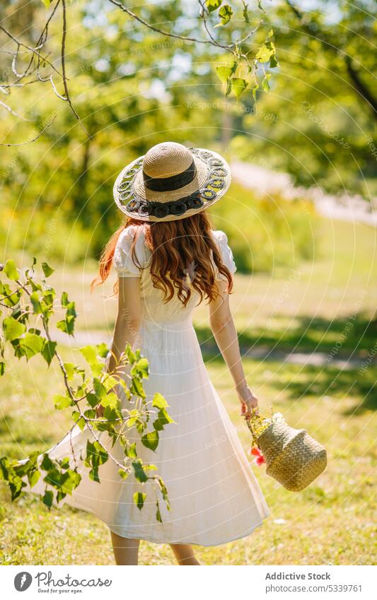 Unrecognizable woman with wicker basket walking in sunny nature lawn field summer countryside tree garden straw hat female lush grassy meadow young sundress