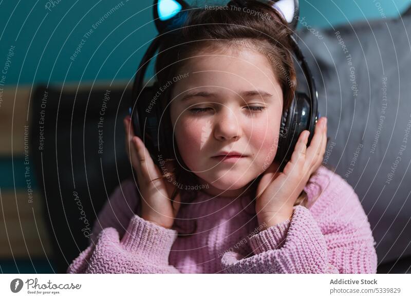Calm child in headphones sitting on bed kid music listen adorable thoughtful bedroom gadget little home device comfort at home calm cozy inside peaceful cute