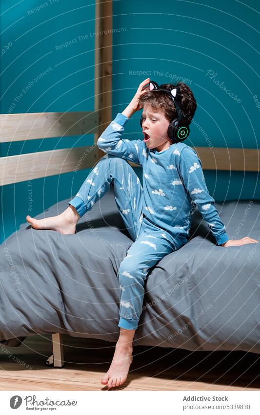 Cute child with headphones sitting on bed kid sing song music listen night wireless cute bedroom gadget childhood home device audio enjoy carefree melody