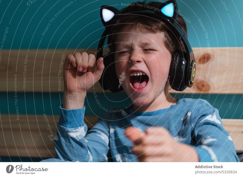 Excited child listening to music with headphones kid sing eyes closed excited scream yell shout clench fist wireless night carefree sound melody joy vivid loud