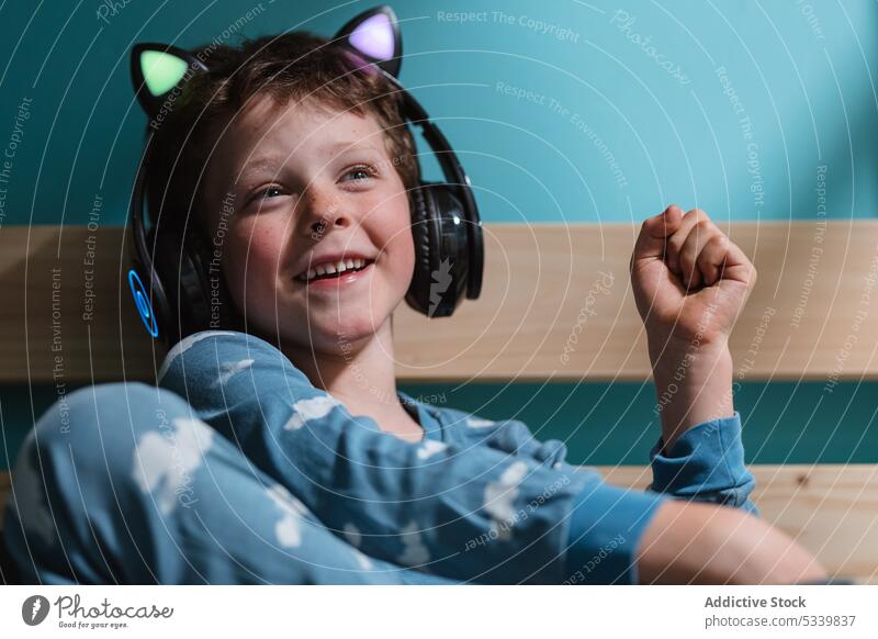 Cute child with headphones sitting on bed kid music listen night smile wireless cute bedroom gadget childhood cheerful home happy device glad audio enjoy