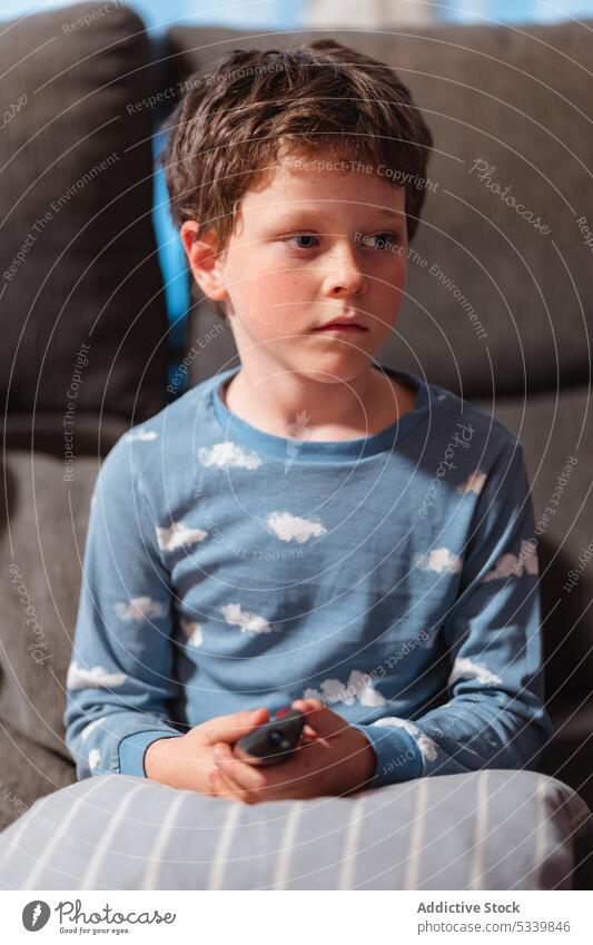 Cute boy with remote controller at home sofa cozy evening pajama couch kid cute adorable portrait living room comfort rest pastime child casual device free time