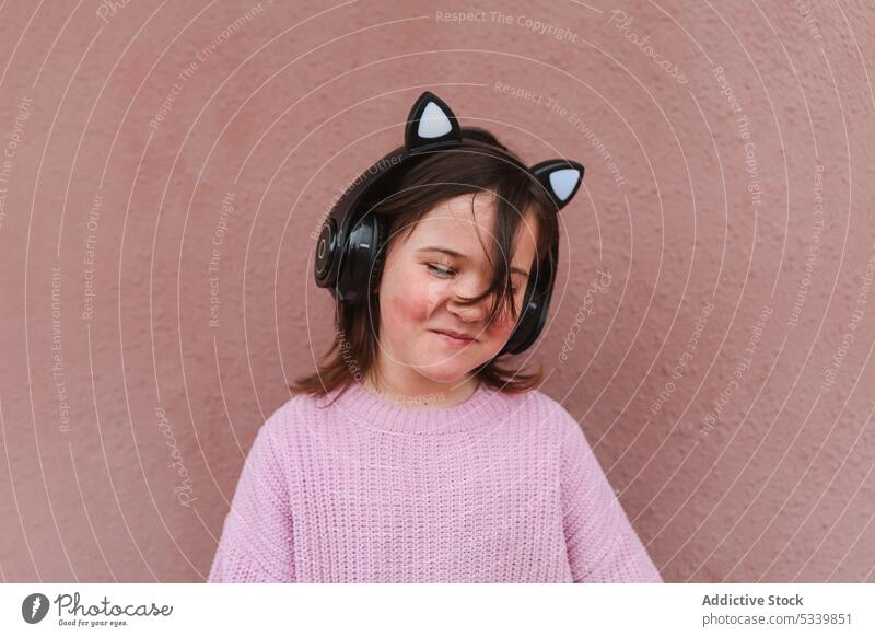 Cheerful girl with headphones against brownish pink wall smile listen music kid portrait happy cute gadget adorable street child sound audio home positive enjoy