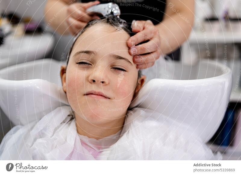 Anonymous hairdresser washing hair of client kid child relax shampoo bowl hairdo water hygiene clean salon head wet hair childhood smile procedure rest sink