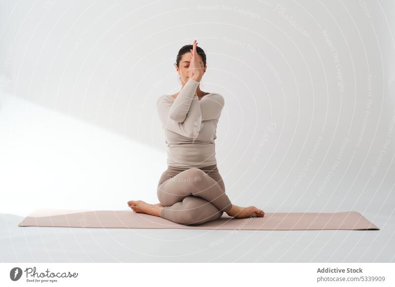 Woman sitting on mat while practicing cow face pose in studio yoga woman meditate practice training barefoot wellness mindfulness wellbeing gomukhasana flexible