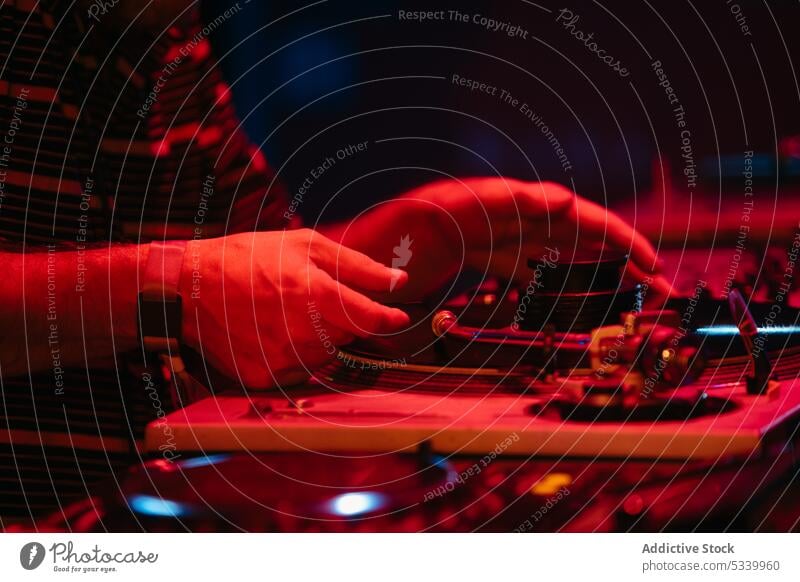 Crop DJ putting on record in red neon man dj party music console night mix equipment entertain play audio professional turntable using perform event panel male