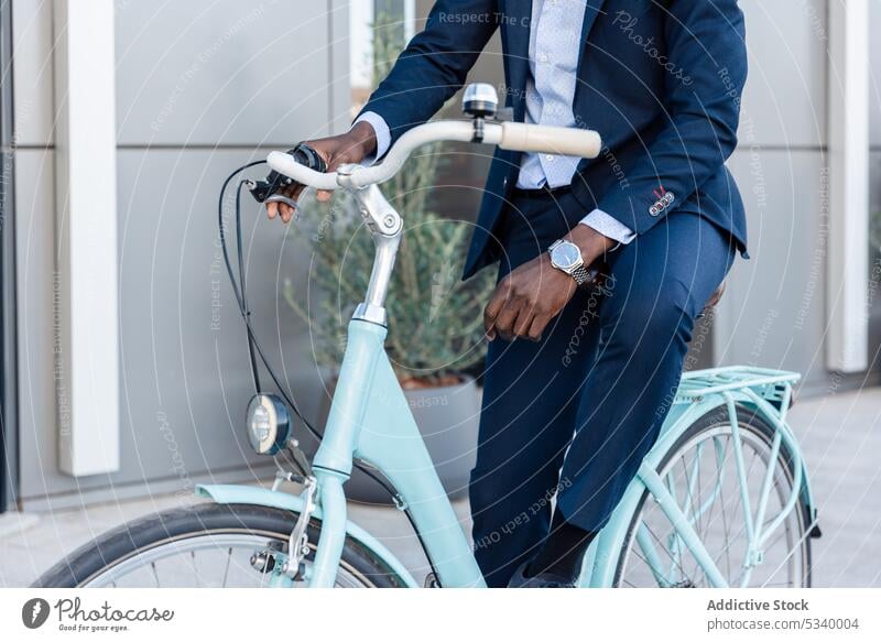Anonymous black businessman riding bicycle in street ride entrepreneur work building african american male well dressed watch ethnic bike contemporary