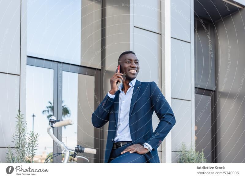 Happy black businessman talking on smartphone while riding bicycle phone call ride conversation discuss cheerful smile street urban ethnic african american
