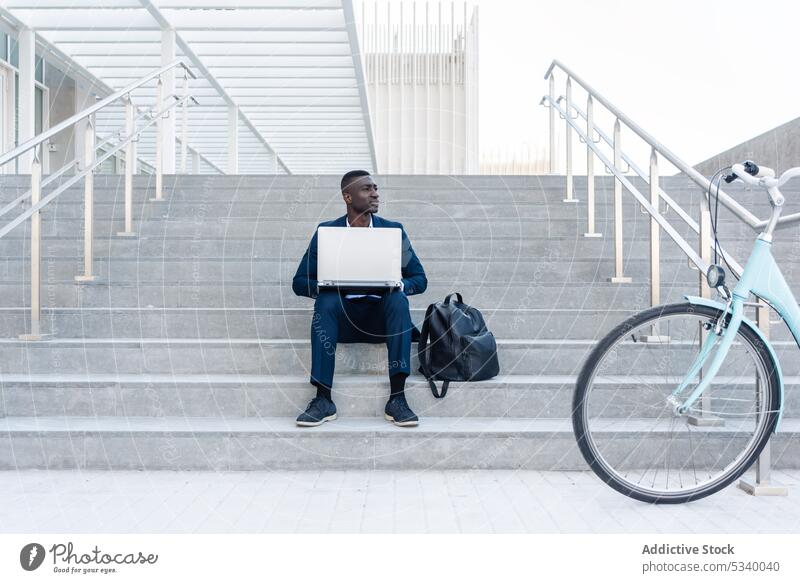 Black businessman working on laptop in street entrepreneur remote typing using freelance job online internet bicycle city african american male ethnic black