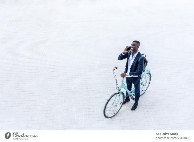 Black businessman with bicycle and backpack talking on phone ride smile cheerful speak communicate positive smartphone street formal male african american young