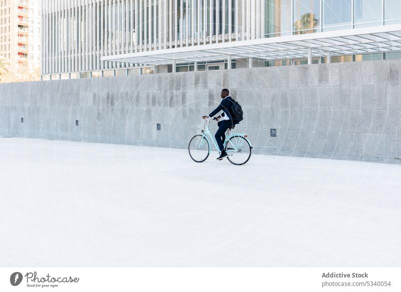 Young black man riding bicycle on street businessman cyclist bike ride entrepreneur employee worker move modern urban wall ethnic male african american