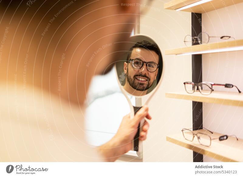 Smiling man looking at mirror during eyewear choice choose customer smile optical select happy glasses store purchase shop client reflection male young cheerful