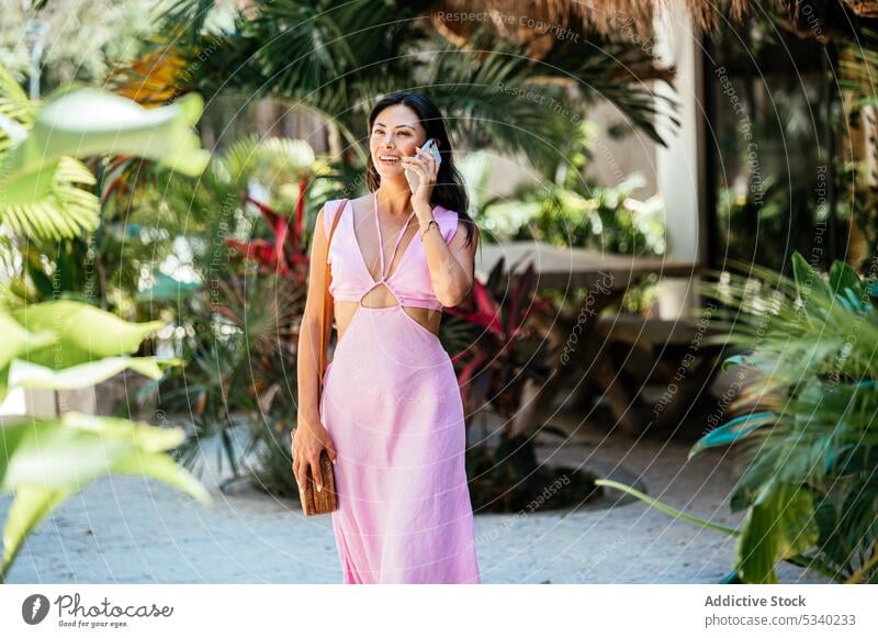 Happy woman talking on smartphone on street with palms garden smile tropical summer speak happy phone call female mexican mexico japanese asian tulum