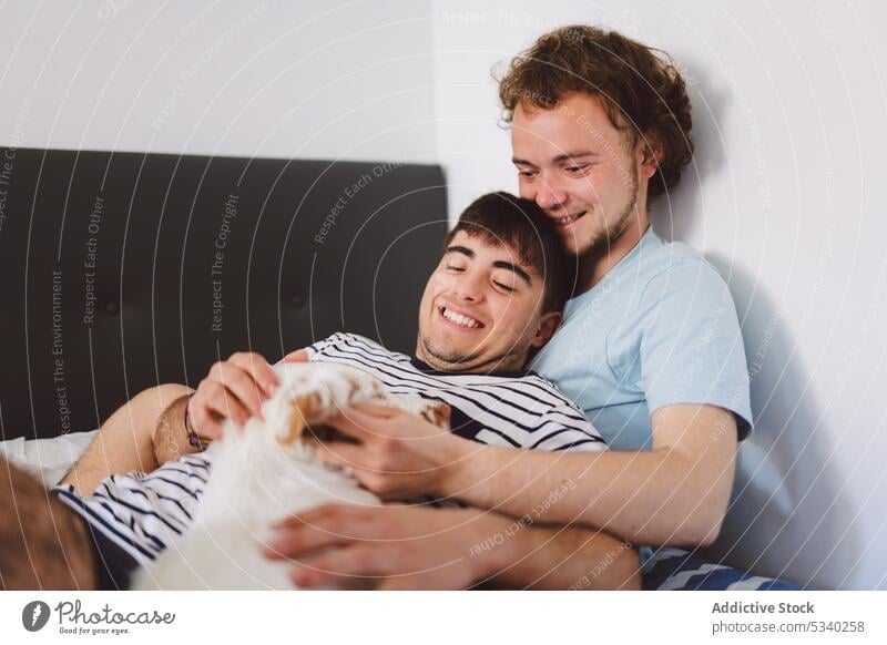 Cheerful gay couple hugging on bed men cuddle relax weekend together home happy love rest lying young smile dog affection relationship lgbt boyfriend homosexual