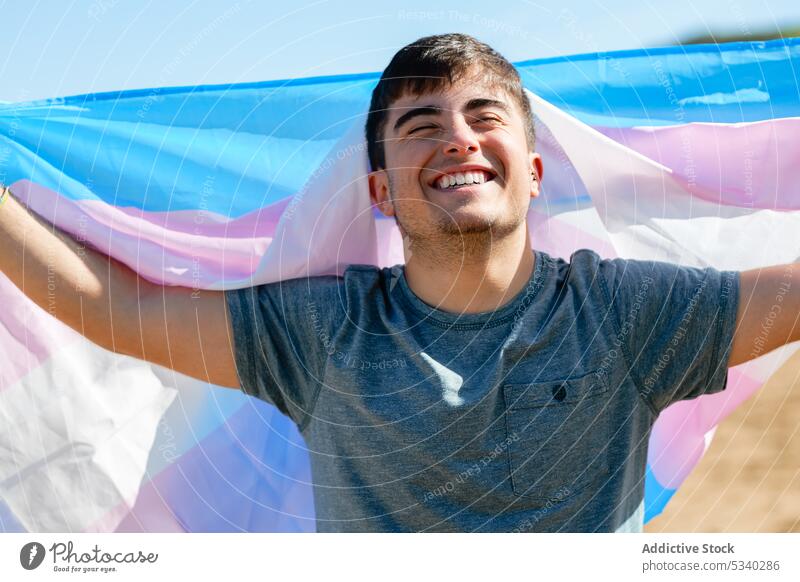 Joyful gay with transgender flag man pride celebrate holiday excited smile beach male lgbt lgbtq homosexual transsexual androgynous queer support tolerance