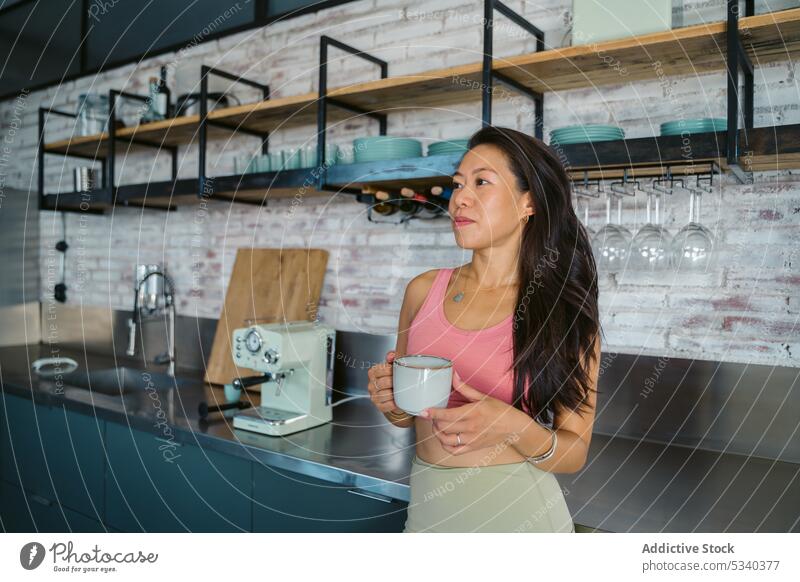 Young Asian woman keeping cup in hands near bar counter in fitness room break drink training wellness sport athlete wellbeing workout sportswoman modern gym