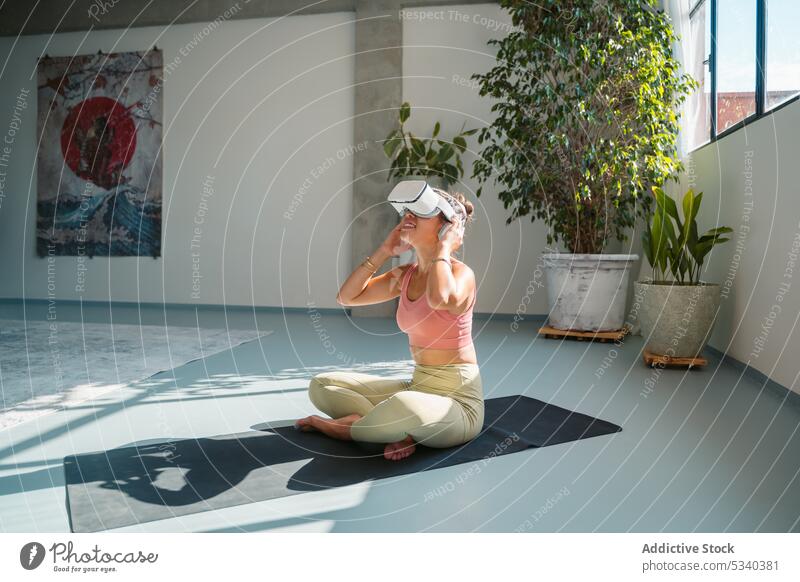 Smiling woman in VR headset on yoga mat vr smile padmasana lotus pose virtual reality goggles cheerful practice wellness barefoot meditate activewear