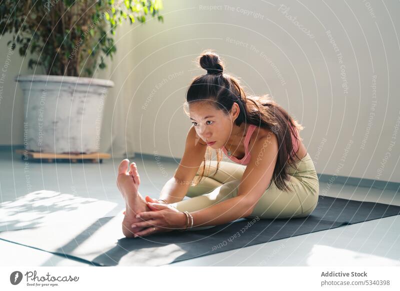 Focused Asian woman stretching in Seated Three Limbed Forward Bend pose yoga asana practice concentrate flexible mindfulness focus young female ethnic asian mat