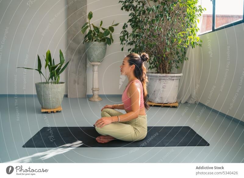 Asian woman in lotus pose on mat in studio yoga padmasana meditate mindfulness zen peaceful stress relief practice young activewear female ethnic asian harmony