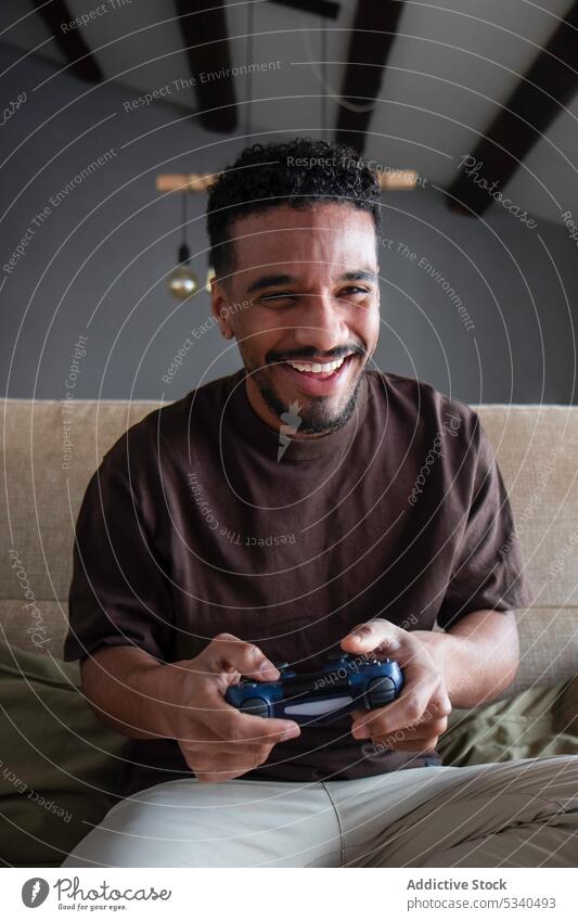 Cheerful ethnic man playing video game on bed videogame joystick gamepad smile weekend happy gamer home african american young cheerful device gadget entertain