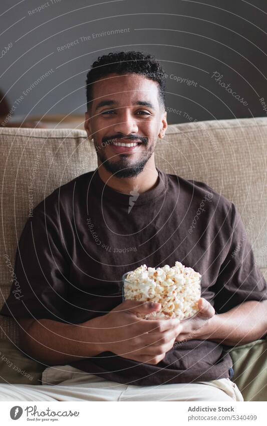 Happy ethnic man eating popcorn and watching TV on sofa tv cheerful weekend home smile african american free time movie rest couch comfort relax living room