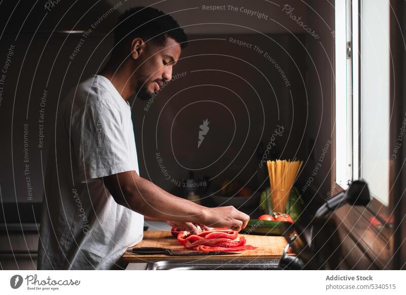 Focused ethnic man cutting bell pepper on chopping board salad knife prepare vegetable kitchen cook healthy food ripe young cutting board vitamin ingredient