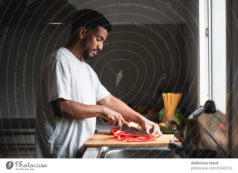 Focused ethnic man cutting bell pepper on chopping board salad knife prepare vegetable kitchen cook healthy food ripe young cutting board vitamin ingredient