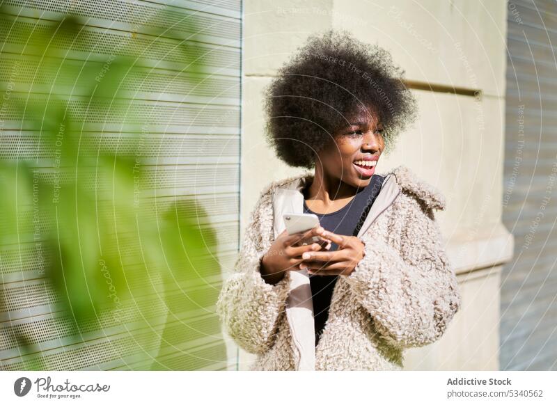 Excited ethnic female with smartphone in town woman texting happy cheerful urban smile cellphone device gadget positive joy african american young lifestyle