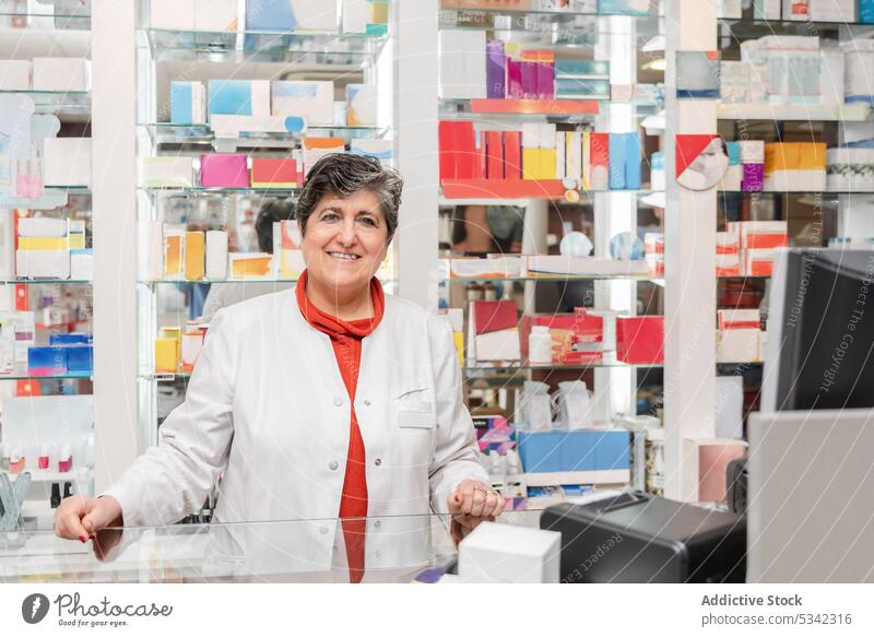 Cheerful woman in medical uniform looking at camera during work drugstore pharmacist pill medicine smile pharmaceutical pharmacy treat showcase female positive