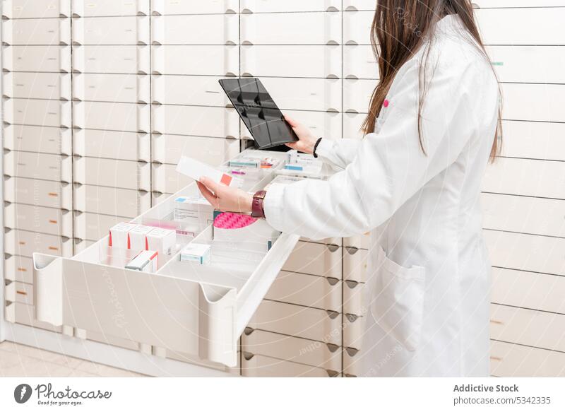 Crop pharmacist using tablet while standing by slotted shelves with drugs in modern store scientist laboratory woman pharmacy drugstore device gadget medication
