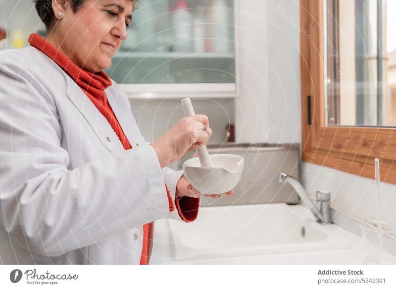 Mature doctor in medical uniform using mortar and pestle during medical preparation woman pharmacist prepare grind ingredient medicine process specialist