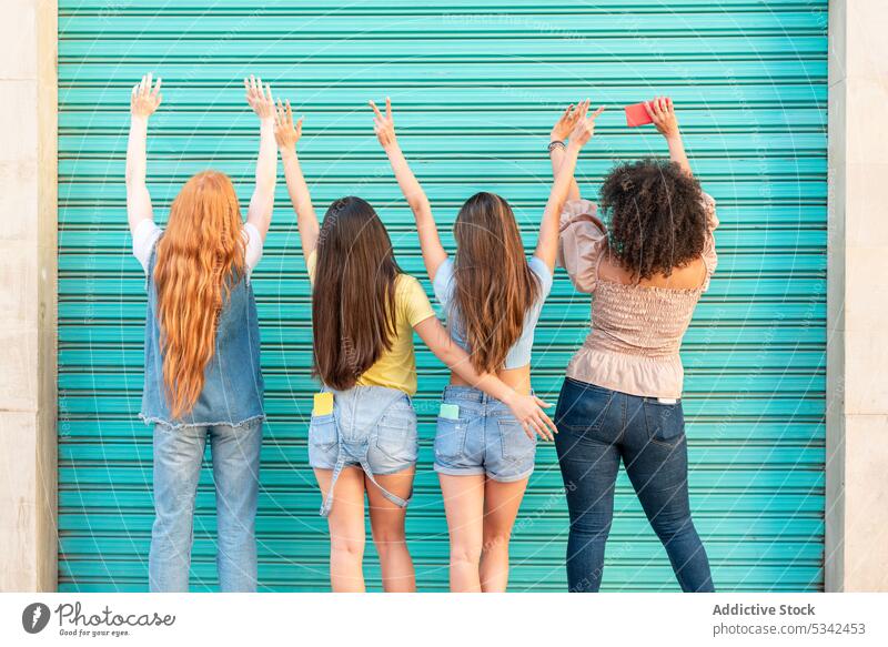 Group of diverse women with hands up against green door friendship together girlfriend street group happy relationship joy arms raised urban multiethnic