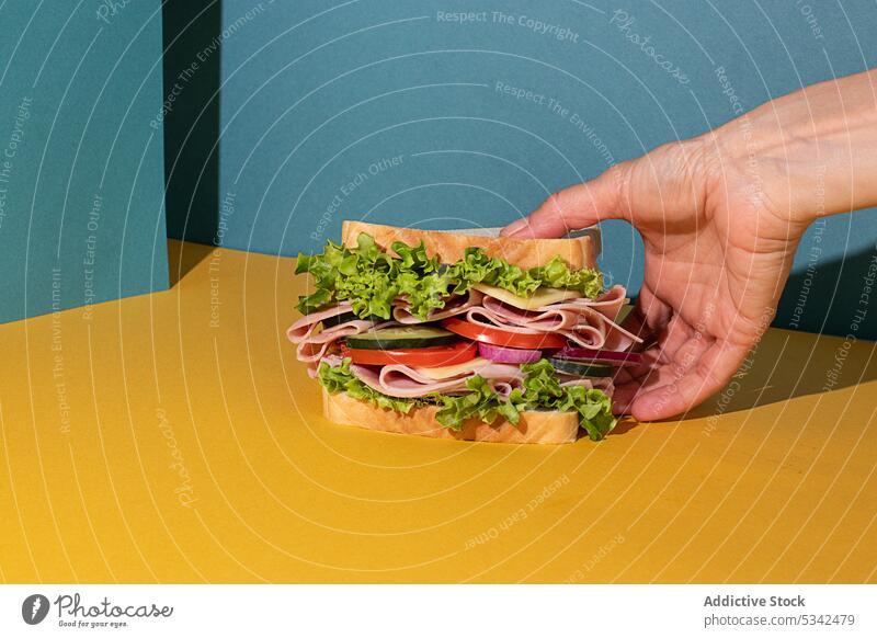 Anonymous person eating sandwich with veggies and ham on colorful background snack homemade stuffed cheese onion lettuce tomato bread food chicken tasty slice