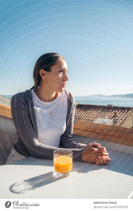 Thoughtful woman drinking fresh orange juice on balcony pensive calm rest relax admire terrace female beverage casual thoughtful enjoy young picturesque
