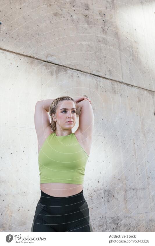 Young sportswoman stretching arms near concrete wall training exercise warm up fitness workout wellness healthy female sportswear young athlete wellbeing