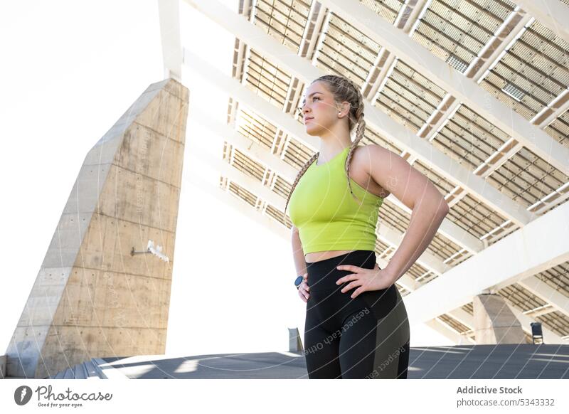 Sportswoman standing under solar panels in city athlete fit sportswear confident construction fitness workout hand on waist training sportswoman stair wellness