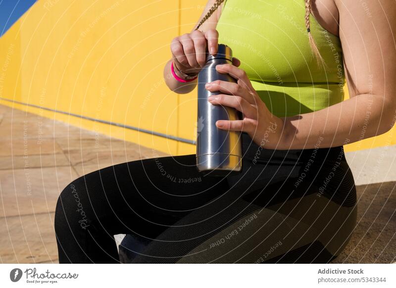 Anonymous sportswoman with bottle of water after training athlete break rest workout relax wall bright sportswear concrete female fitness sporty wellness