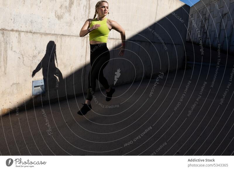 Fit sportswoman jogging on asphalt road by concrete wall athlete sportswear shadow run training wellness street young lady female runner exercise vitality