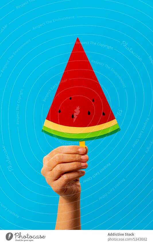 Crop anonymous person showing slice of artificial watermelon popsicle demonstrate fruit summer yummy sweet creative hand paper bright fresh tasty colorful