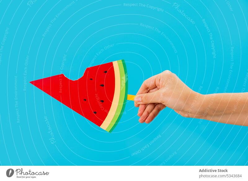 Crop anonymous person showing slice of artificial watermelon with a bite out popsicle demonstrate fruit summer yummy sweet creative hand paper bright fresh