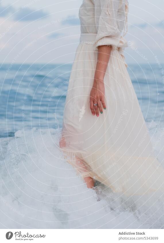Anonymous woman in dress walking in sea water seashore summer ocean holiday beach nature vacation wave blue sky female coast cloudy harmony seascape resort calm
