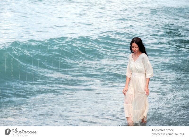 Calm woman walking in waving sea during summer vacation beach water dress ocean seashore turquoise charming female nature coast holiday young travel enjoy calm