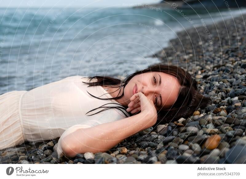 Charming woman lying on stony seashore summer rest vacation smile coast wave happy beach ocean positive relax female stone water young cheerful carefree travel