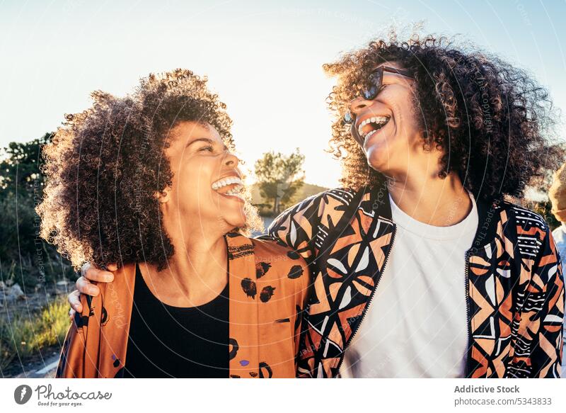 Cheerful girlfriends laughing while having fun during daytime women park friendship road bonding happy cheerful summer female positive joy smile curly hair