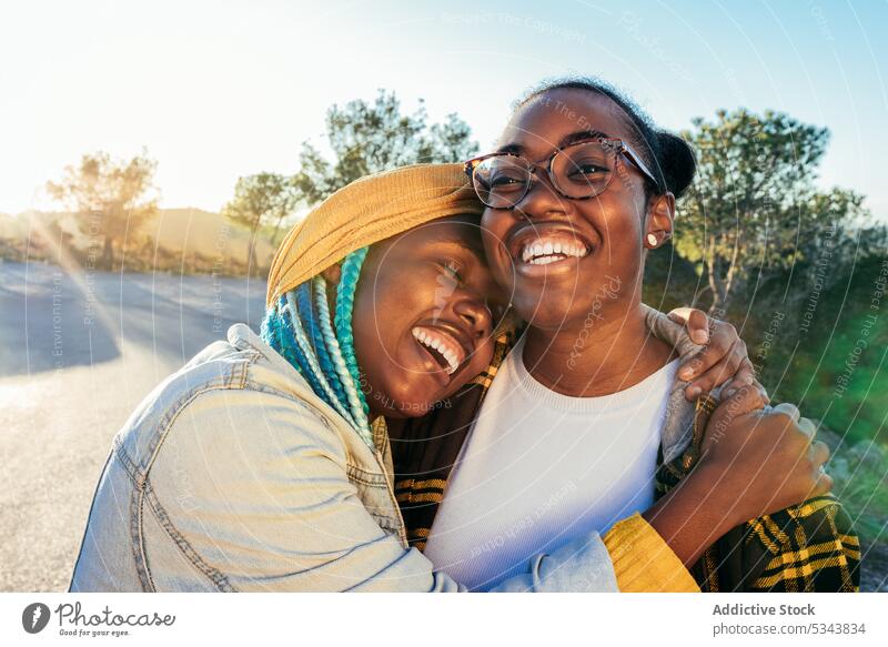 Cheerful black women hugging on road in countryside friend embrace laugh cheerful friendship nature leisure weekend african american ethnic eyes closed