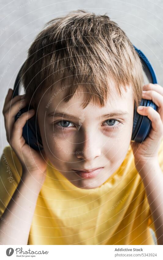Front view of cute kid looking at camera while listening to music beautiful boy child ear eyes face headphones human over-ear person portrait t-shirt teenager