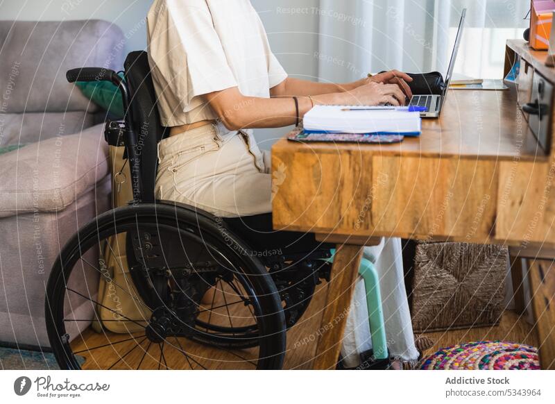 Cropped body of young woman sitting on wheelchair while taking notes from laptop notebook take note write freelance sofa living room home using gadget at home